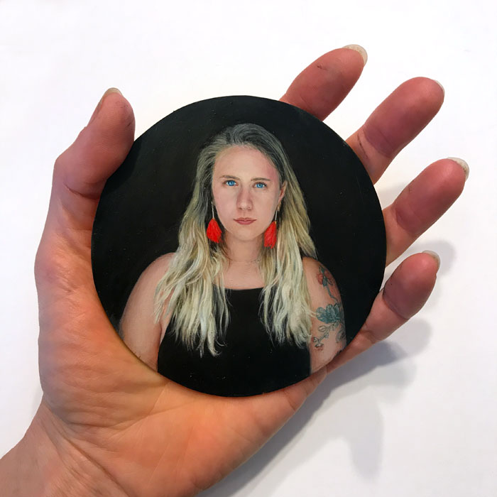 Artist Rebecca Luncan holding her miniature portrait painitng of young woman